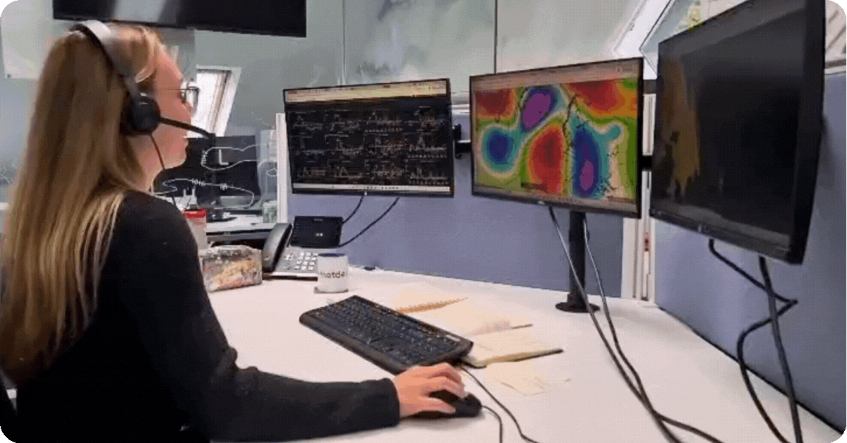 A GIF of an energy meteorologist hosting MetDesk LIVE on their computer. They are on the phone using a headset looking at 3 screens with Trading Weather on them. 